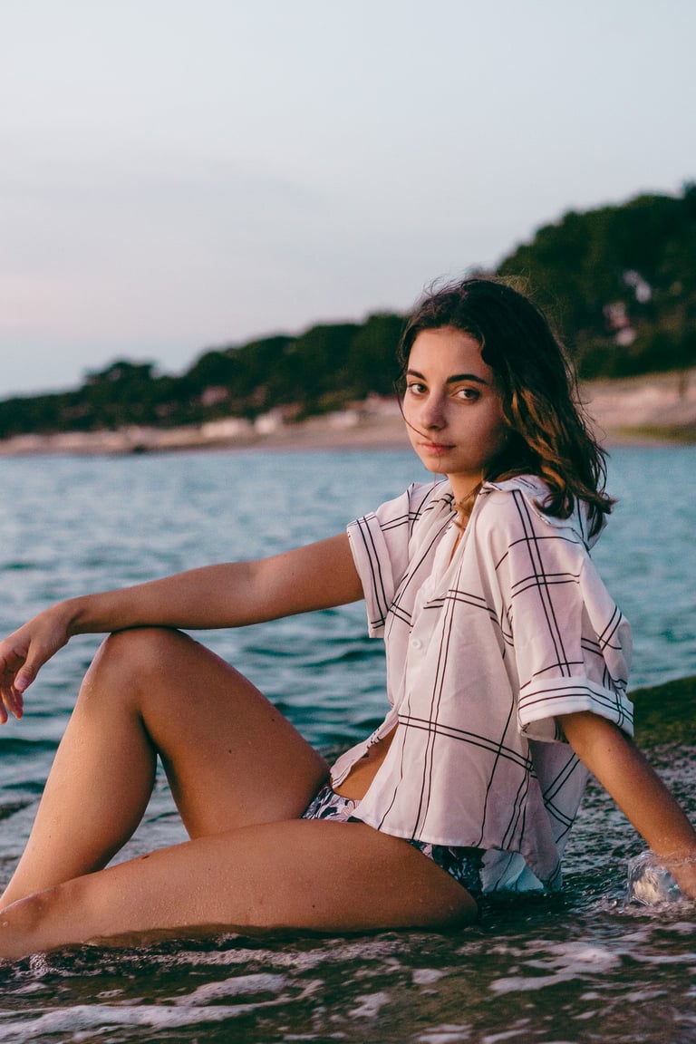 femme assise sur la plage portant une chemise et un maillot de bain regardant l'objectif