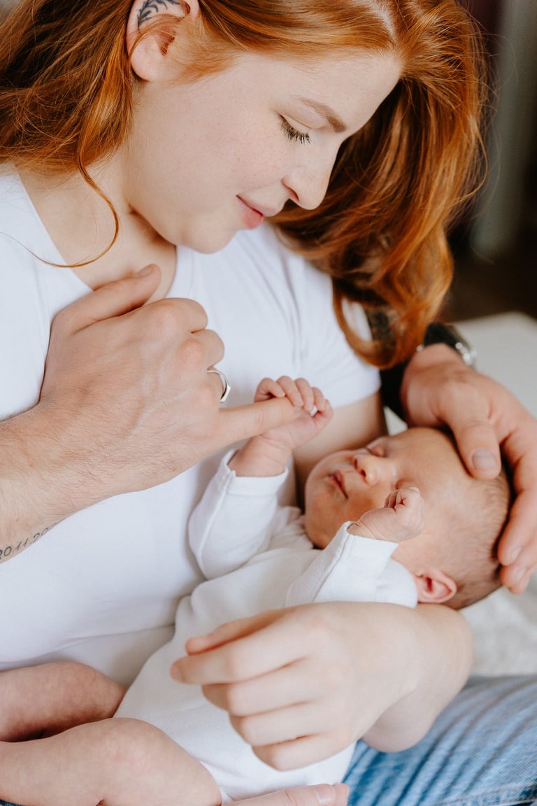 plan rapproché d'un bébé dans les bras de sa mère qui tiens un doigt de son père