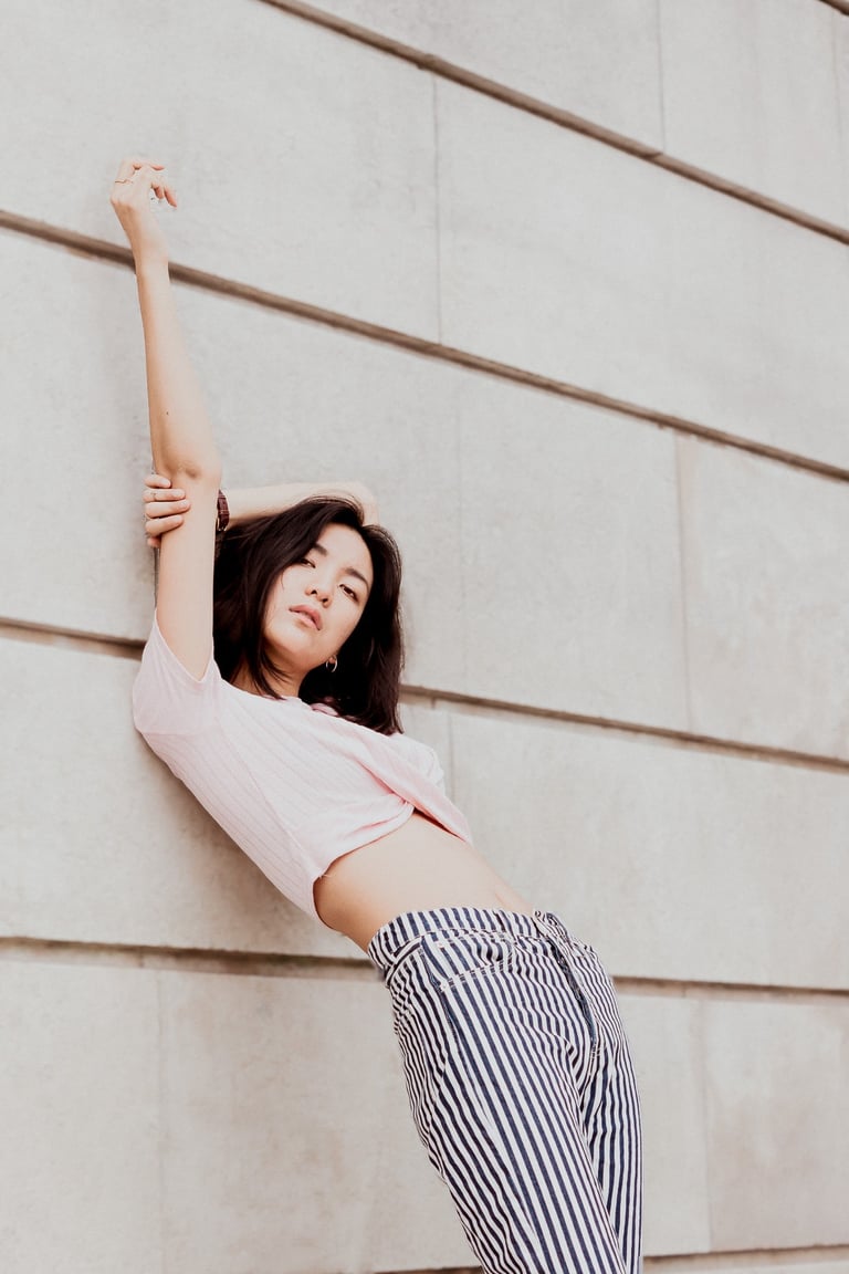 portrait de femme adossée contre un mur en pierre le bras en l'air couleur douces
