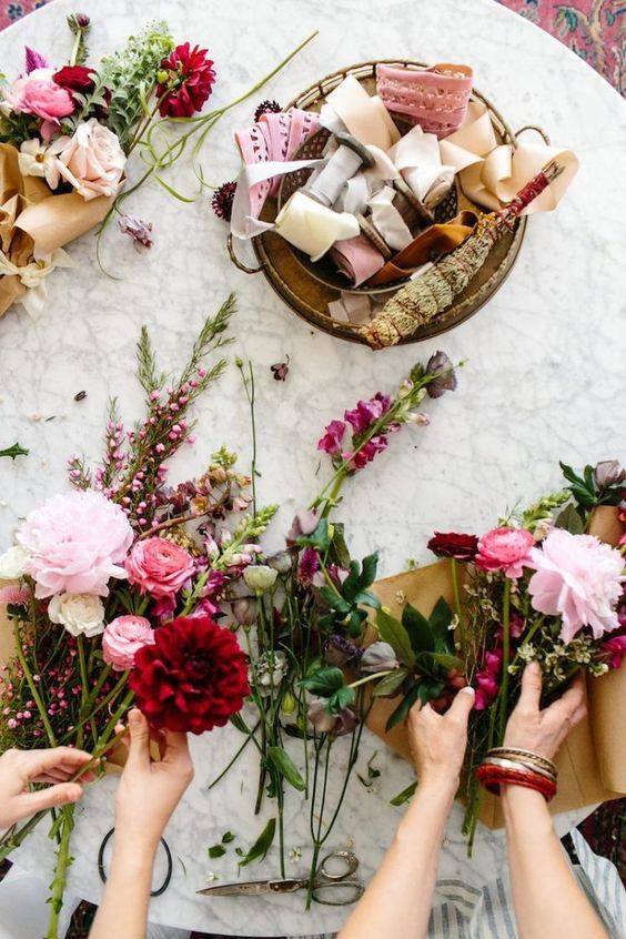 Manos creando una guirnalda floral con rosas y dalias.