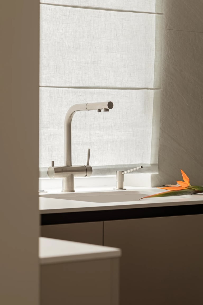 Detal kuchni: bateria stalowa pod oknem, lniana roleta rzymska.