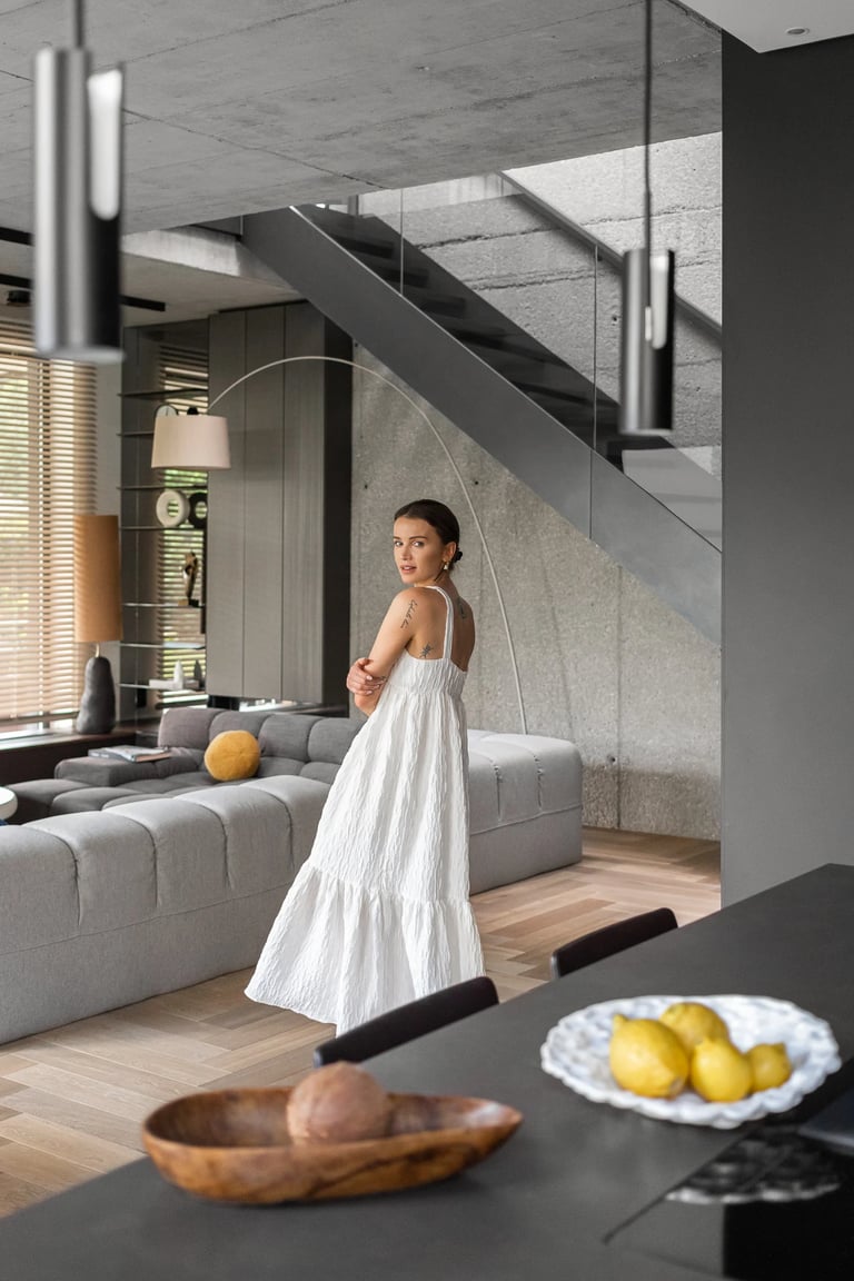 Fotografia wnętrz lifestyle, kobieta w białej sukience na tle betonowych schodów w domu.