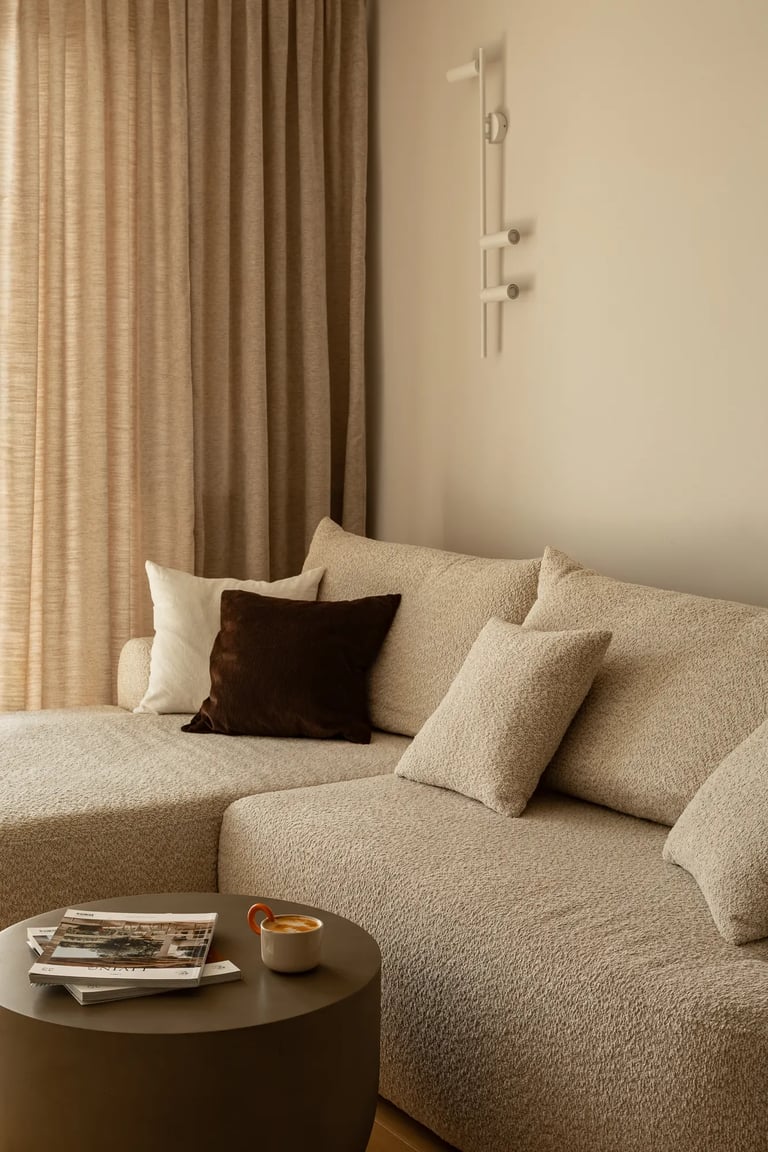 Beżowa narożna sofa boucle i brązowe poduszki w przytulnym salonie.