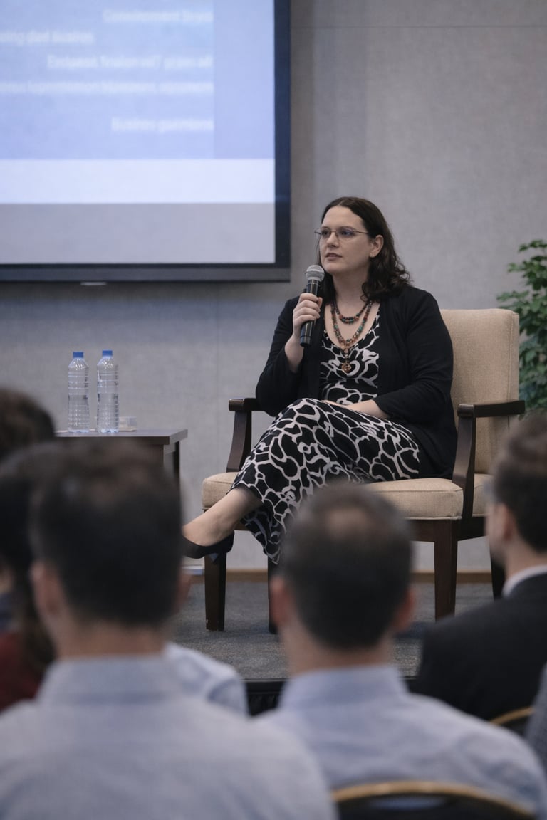 Female speaker holding a microphone while addressing an audience at a business conference panel.