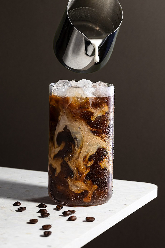a glass of iced coffee with a pitcher of milk