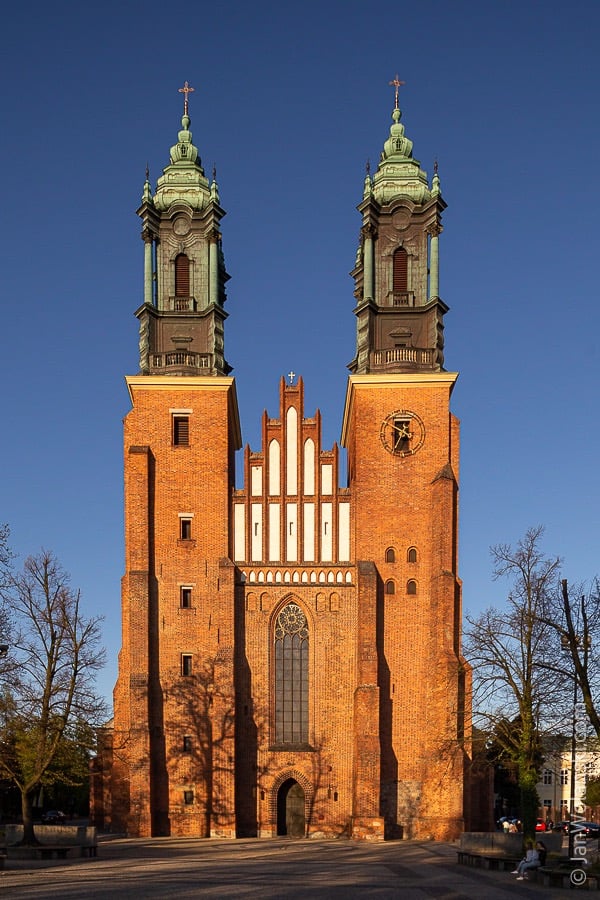 Zdjęcie przedstawia imponujący, ceglany budynek kościoła z dwoma wysokimi wieżami, które dominują nad główną nawą.