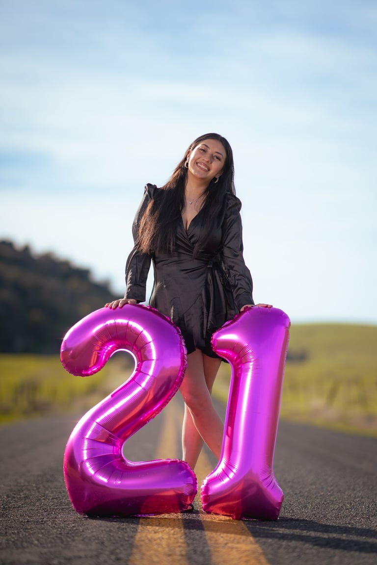 Creative 21st birthday portrait in Visalia with large pink balloons on a scenic open road.