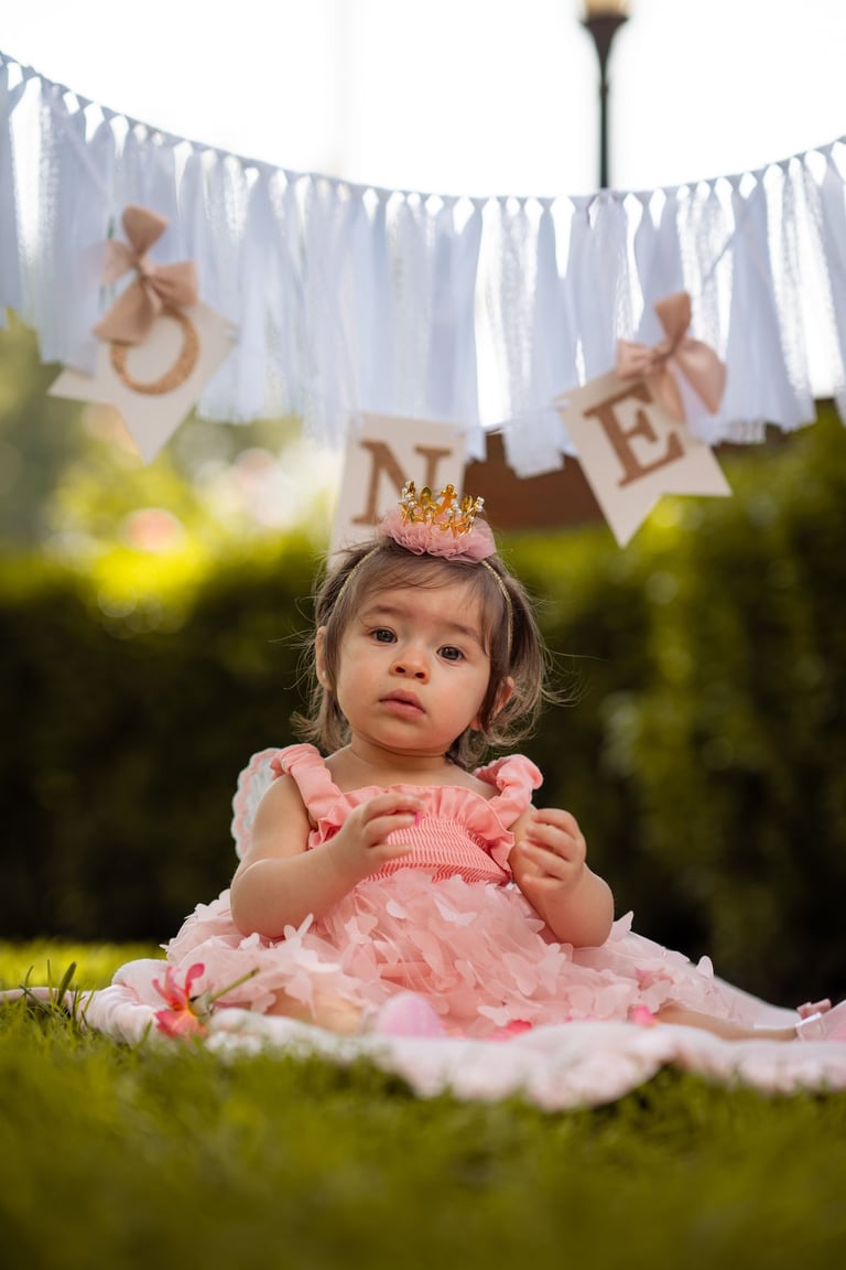 Visalia cake smash and first birthday photographer featuring a baby girl in a pink dress outdoors.