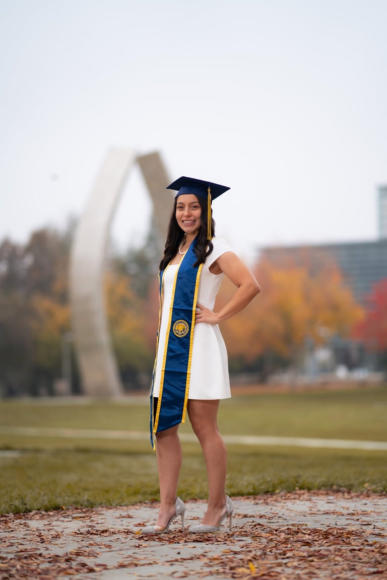 Graduation portrait at UC Merced featuring a senior in a white dress and cap in front of the statue