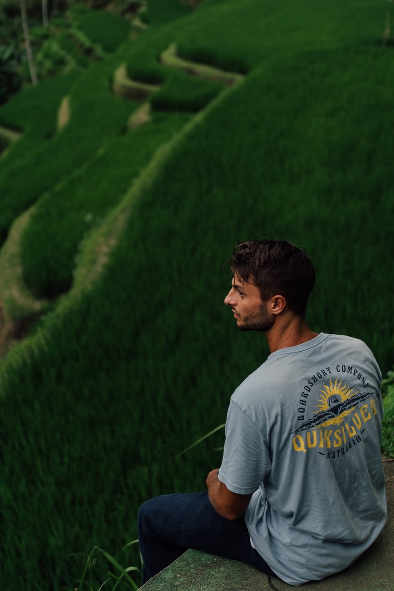 a man sitting on a ledge looking out over a rice field