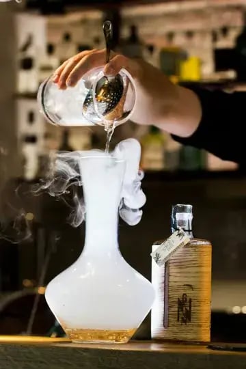 a person pouring a drink into a glass vase