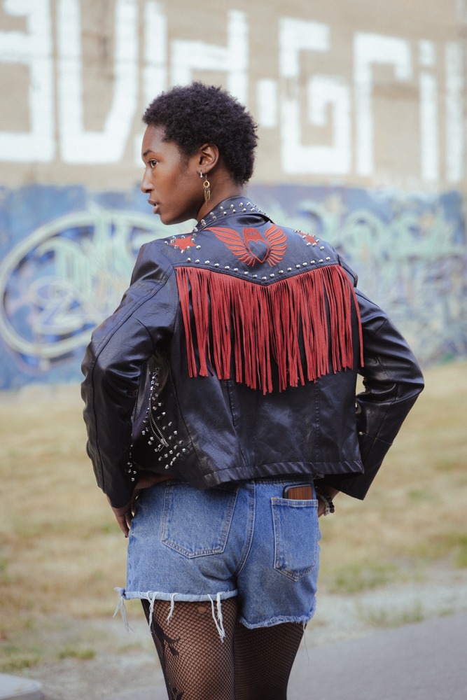 Fuller image of model looking over her shoulder, cool earrings and black denim jacket.