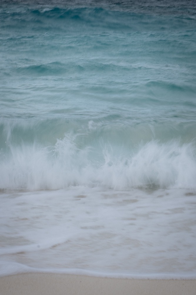 Slow shutter image of waves crashing on beach, pastel blues.