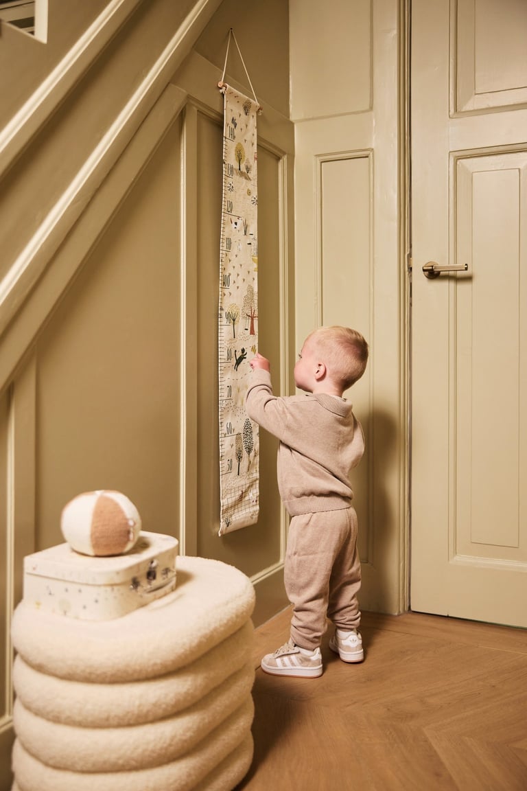 A young toddler looking at a height chart, in a Jollein photoshoot