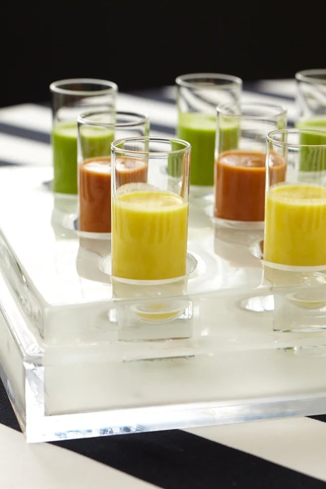 Colorful vegetable soup shooters in small glass cups on a clear acrylic serving tray.
