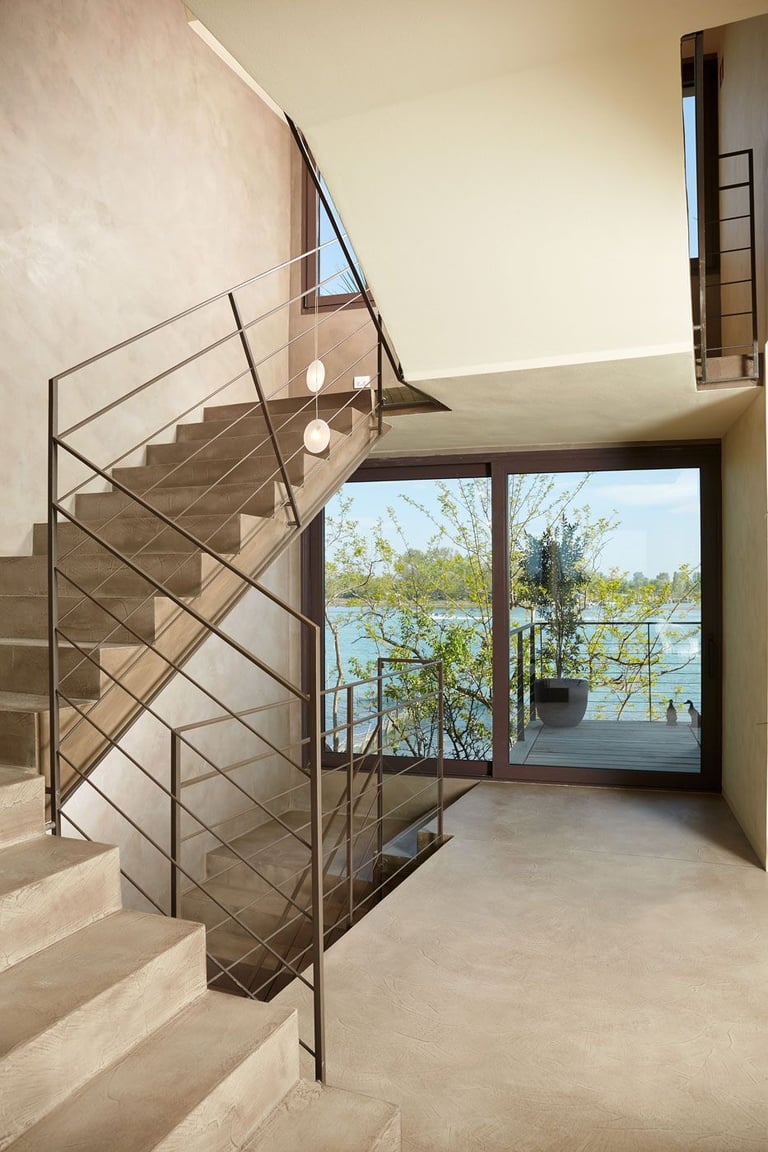 A modern staircase in microcement with metal handrails, offering views of a picturesque lake through
