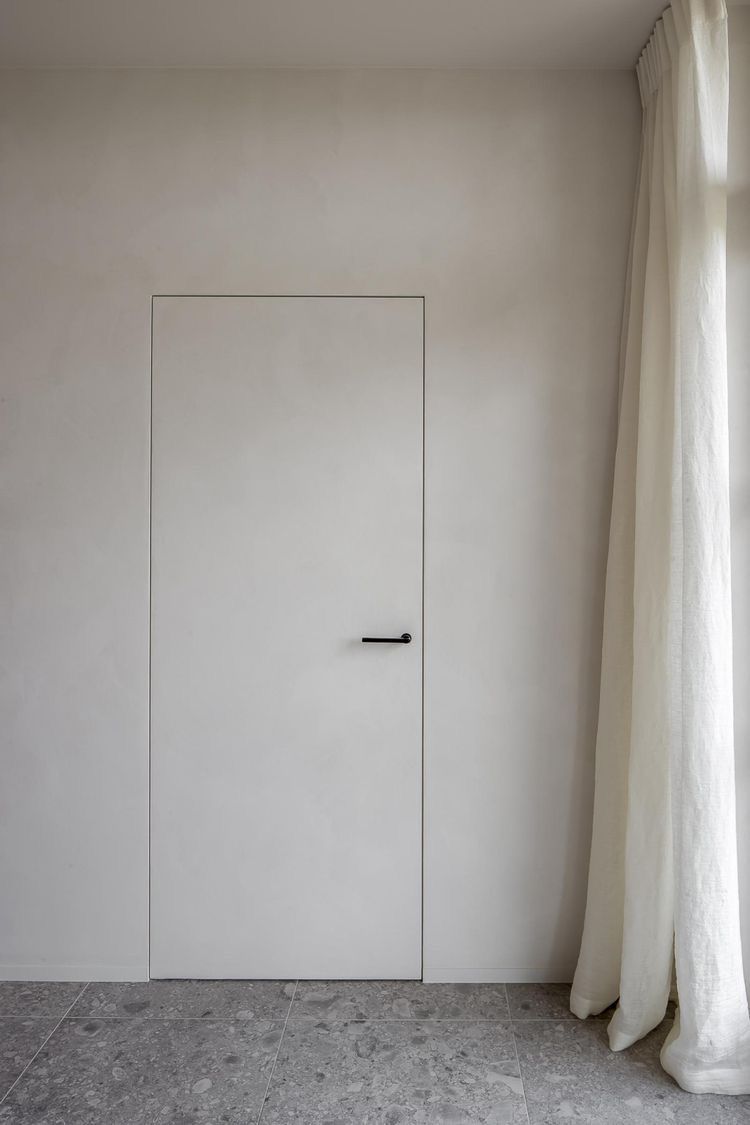 Minimalist white interior door with microcement finish, black handle and stone tile flooring.