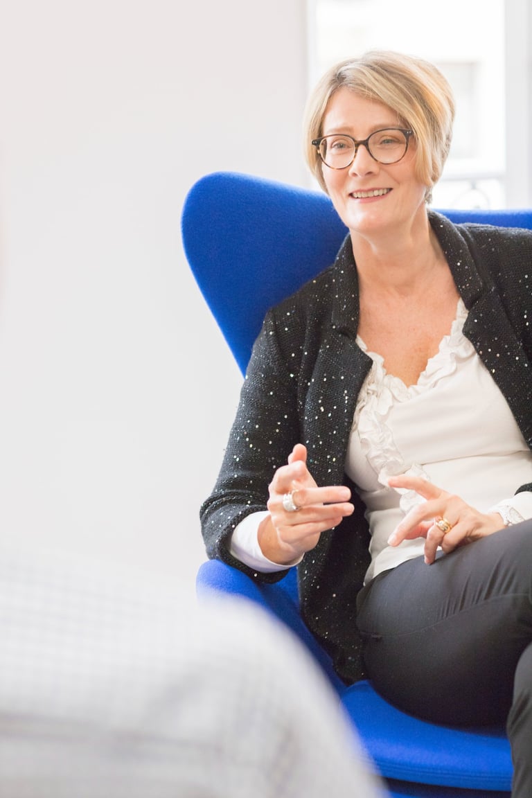a woman in glasses and a black jacket sitting in a chair