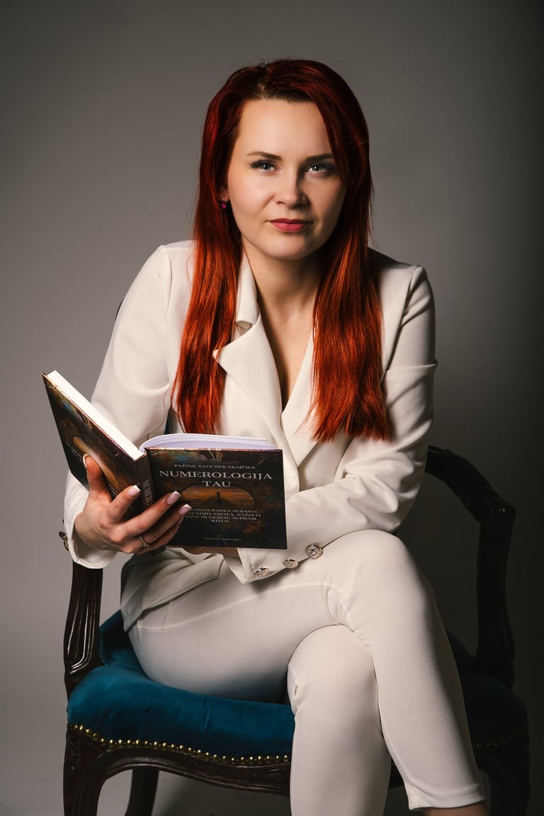 Numerologės Jolantos profesionalus portretas su knyga „Numerologija Tau“, simbolizuojantis jos ekspertines konsultacijas, ska