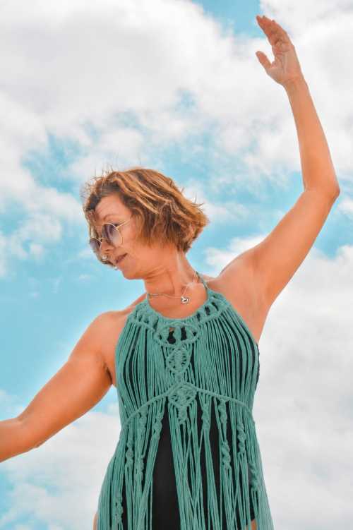 Una muje con vestido de macrame de playa con flecos de macramé verde y gafas de sol bailando 