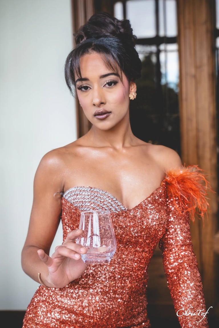 Photo à Perpignan d'une femme élégante en robe orange tenant un verre, chignon haut et maquillage