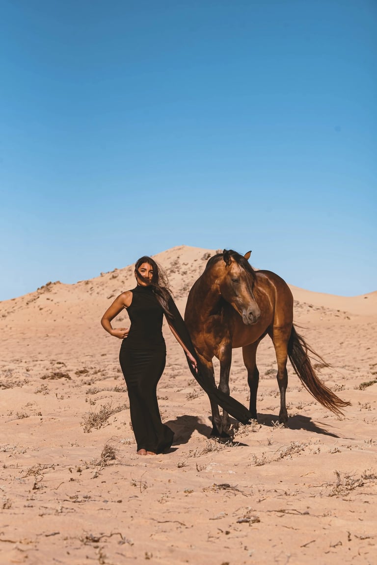 Editorial photography in Dakhla desert with a fashion model and a brown horse against a clear blue Sahara sky.