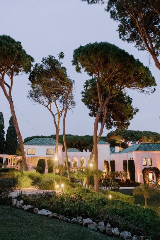 Villa El Rincon exterior with tall pine trees illuminated at dusk