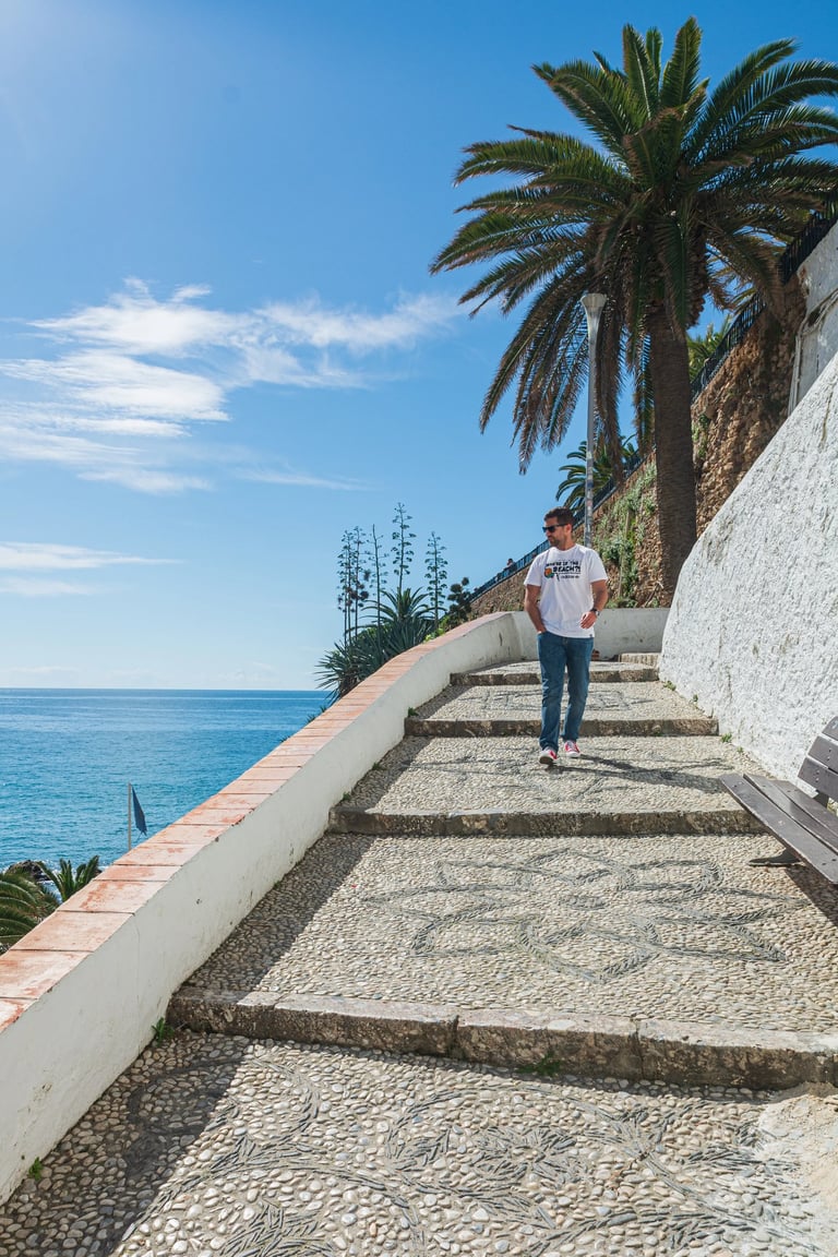 A man walks down a scenic cobblestone coastal path in Spain overlooking the Mediterranean Sea.