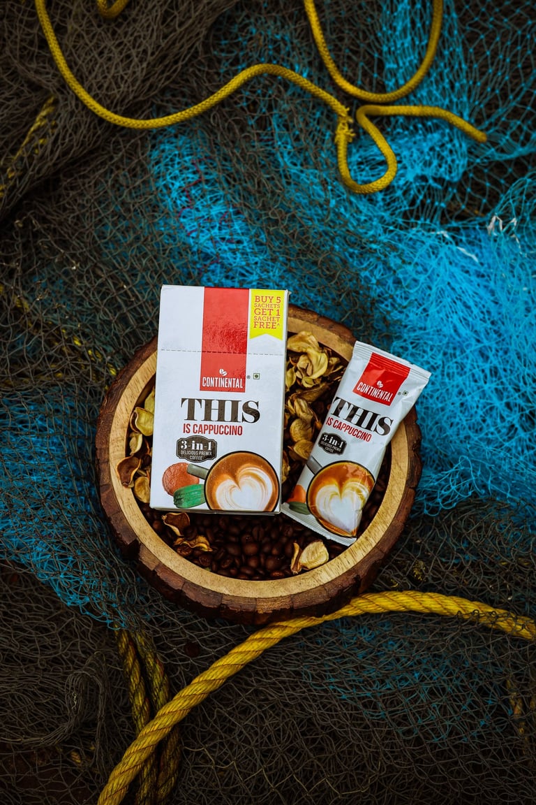Continental This Is Cappuccino 3-in-1 instant coffee premix box and sachet on a rustic wooden bowl.