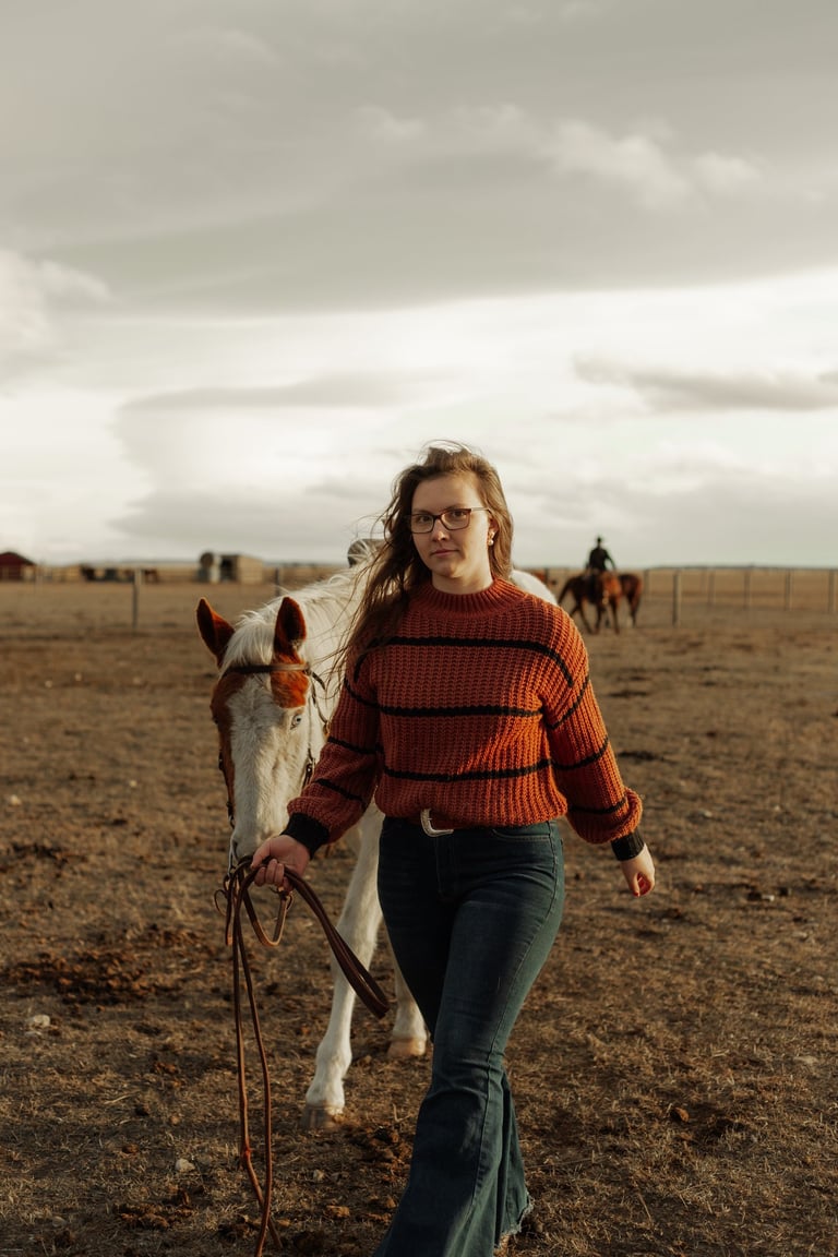 a woman in a red sweater and jeans walking with a horse