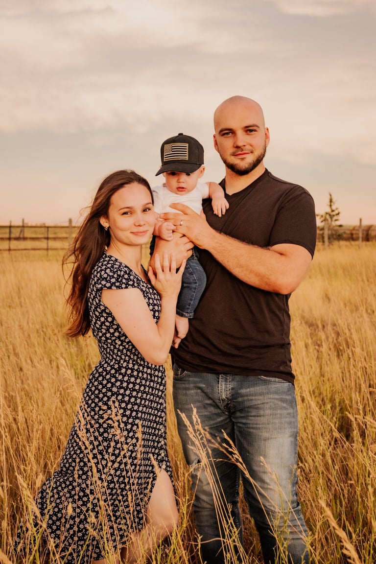 a man and woman standing in a field holding a baby