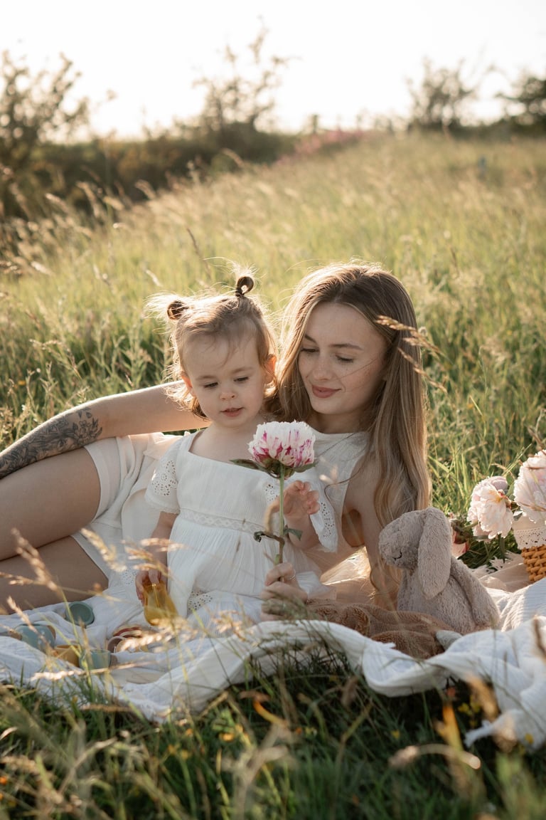 A mother and young daughter in white dresses enjoy a summer picnic in a sunny meadow.