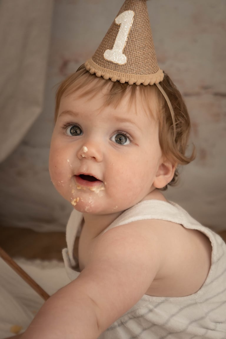 Baby boy celebrating his first birthday cake smash wearing a burlap party hat.