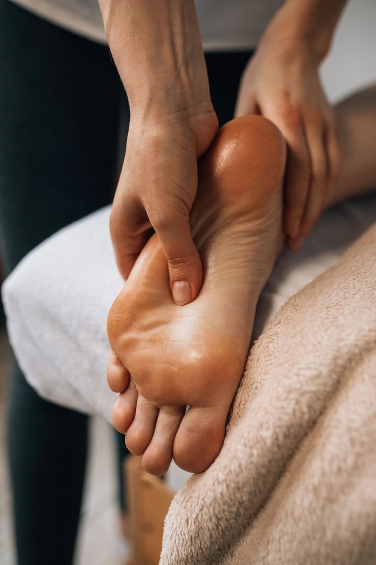 Une personne bénéficiant d'une séance de réflexologie, détendue, assise sur une chaise avec un thérapeute à ses pieds.