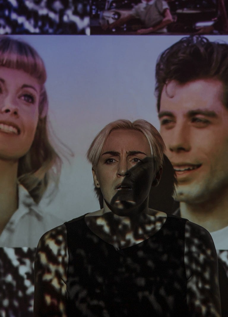 Mary performs during the Adelaide Fringe. She stands in front of a projection of Greese characters