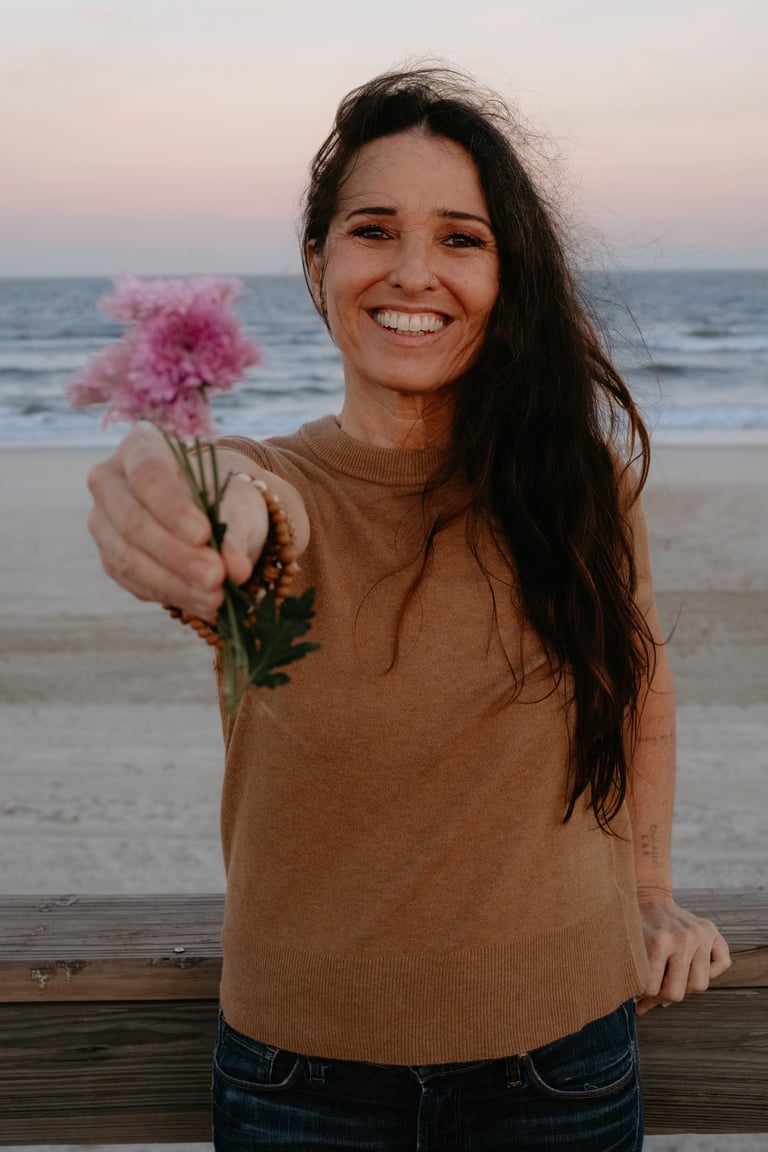 Michael Alexa Pitts on a beach near sunset, smiling, a pale blue ocean, a pale pink sky, offering you a few lavender flowers