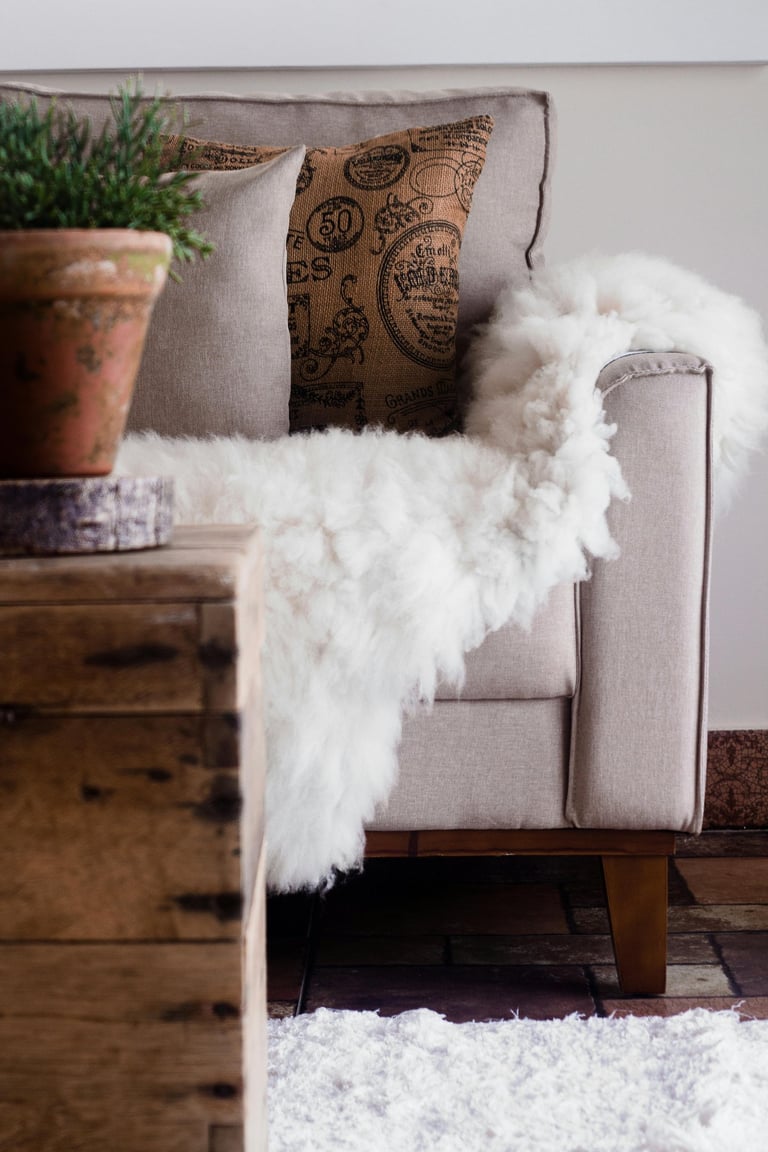Cream upholstered chair styled with patterned throw pillow and faux fur throw blanket