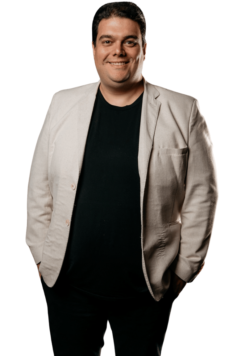 Danïel Sbeghem portrait of a smiling man in a beige blazer and black shirt against a dark background