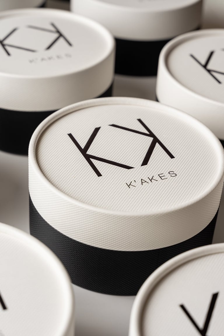 Elegant round black and white K'AKES luxury bakery boxes with minimalist logo branding.