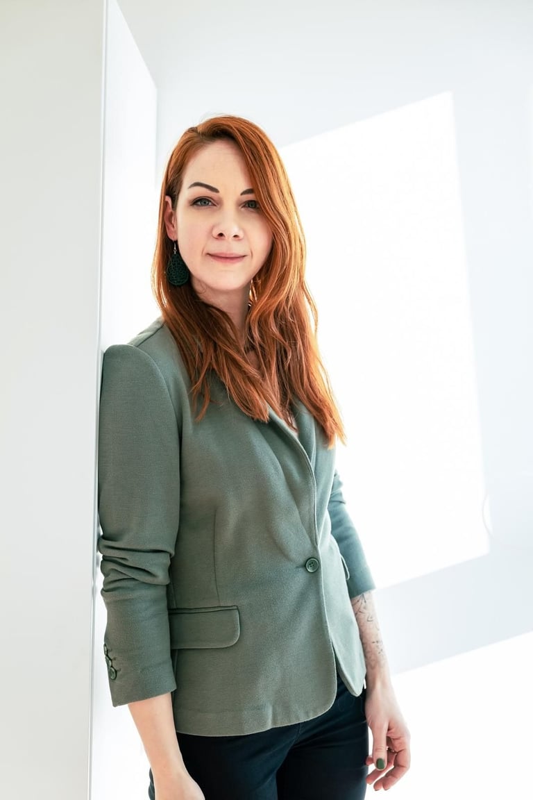 Professional woman with red hair wearing a green blazer in a bright, modern office.