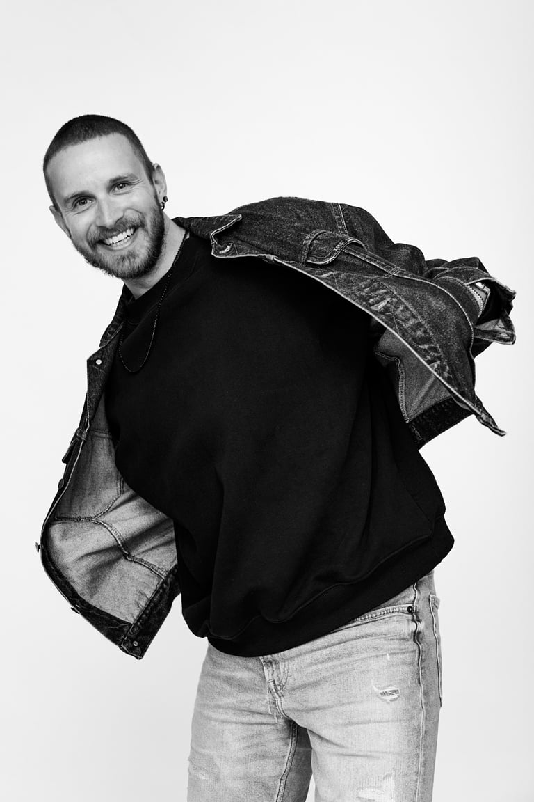A young man smiling in a photo studio wearing a jean jacket.