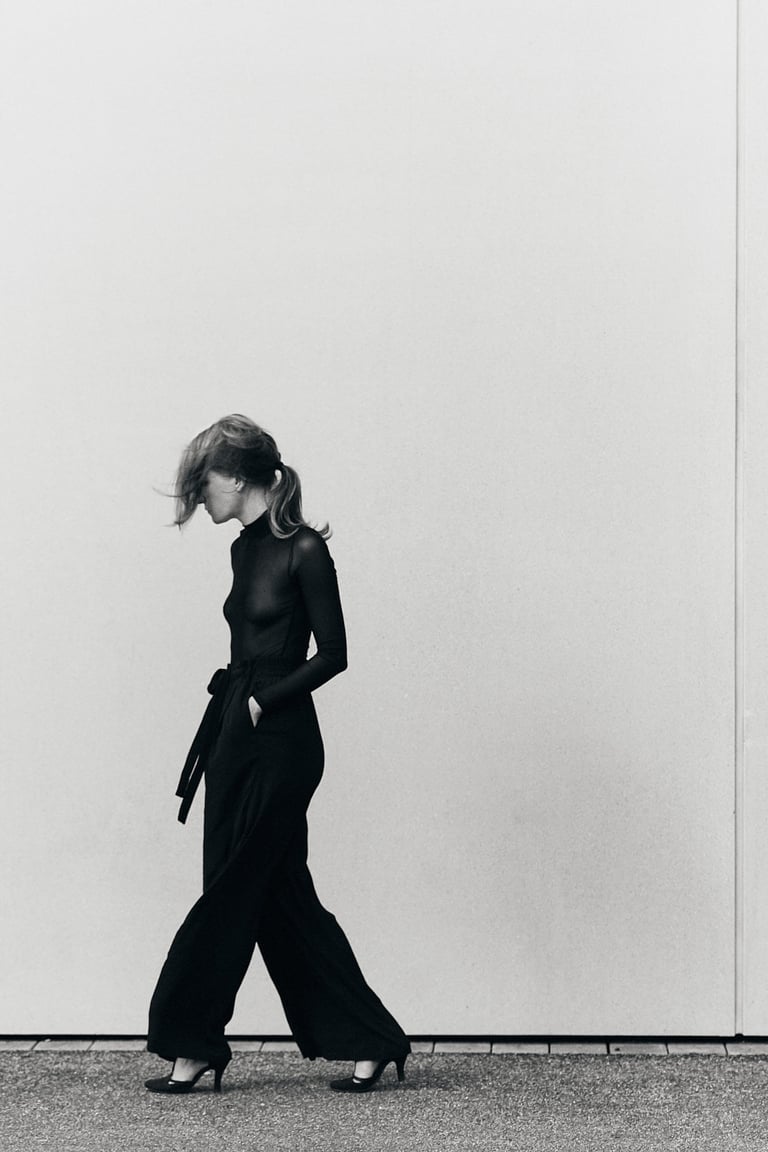 A young woman walking next to a wall in black clothes.
