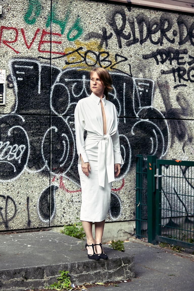 Eine Frau in einem weißen Kleid steht vor einer Wand mit Graffiti.