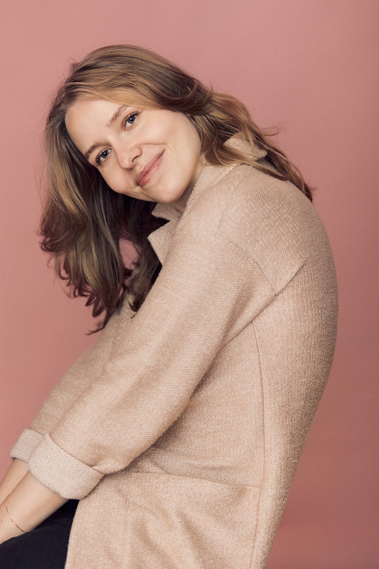 A blonde woman photographed in front of a pink background.