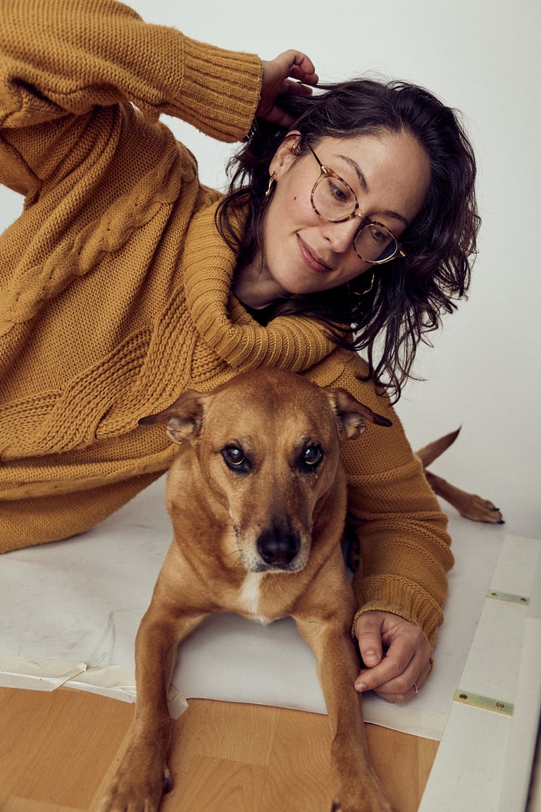 Eine Frau in einem senffarbenen Pullover liegt auf der Seite mit einem Hund.