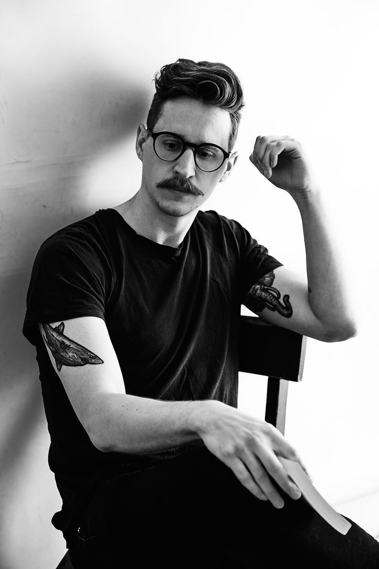 Ein Mann mit Tattoos, der eine Brille trägt und ein Buch in der Hand hält.