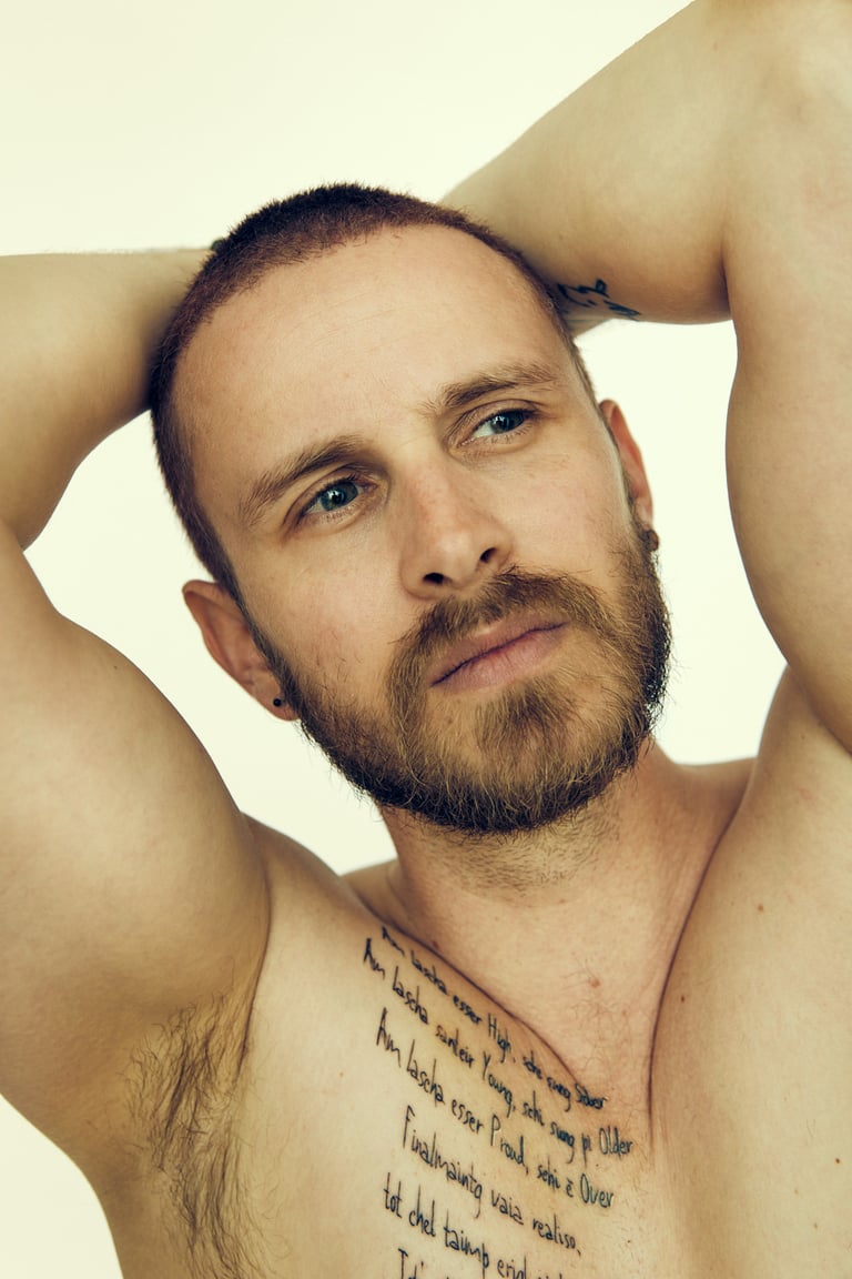 A shirtless man with a tattoo looking to the side.