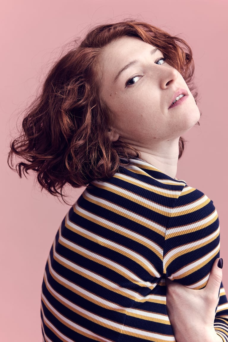 A headshot of a young woman with red hair wearing a striped shirt.