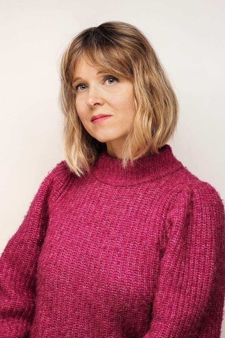 A portrait of a woman in a pink sweater photographed in a studio.