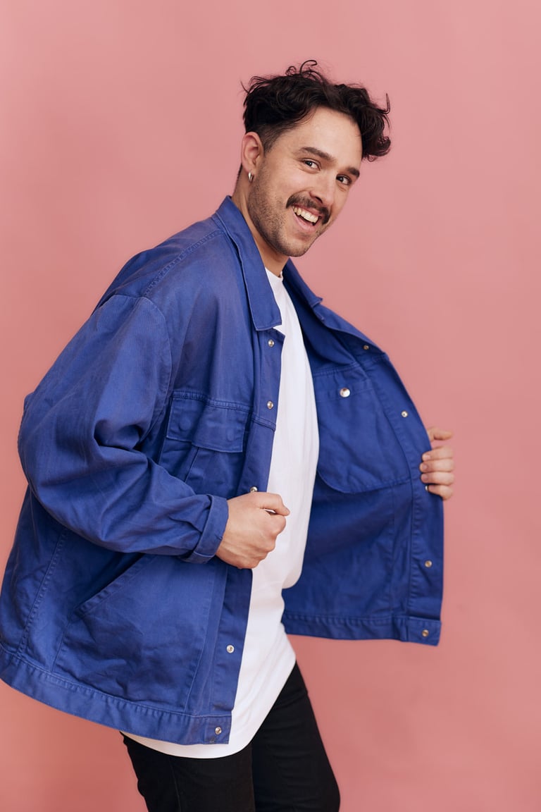 Ein junger Mann mit Schnurrbart, der eine blaue Jacke trägt.